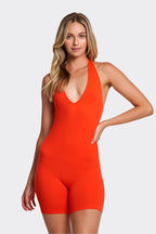 Woman wearing a bright orange halter neck jumpsuit on a plain background