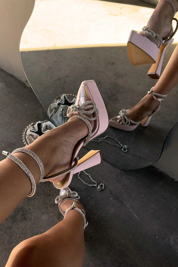 Close-up of high-heeled shoes with platform and decorative elements on a reflective surface.