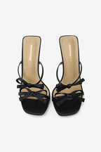 A pair of black high heel mules with square toes and multi-bow details on the straps.