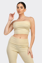 Woman wearing a light yellow strapless top and pants on a white background