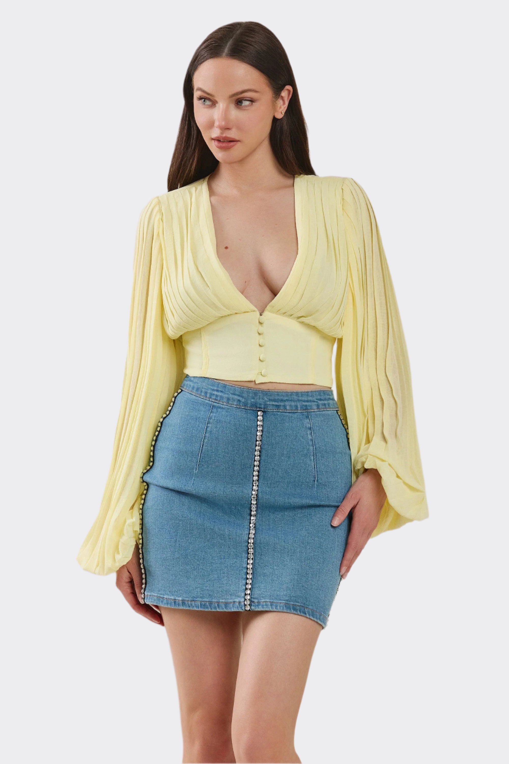 Woman wearing a yellow top and blue denim skirt on a plain background