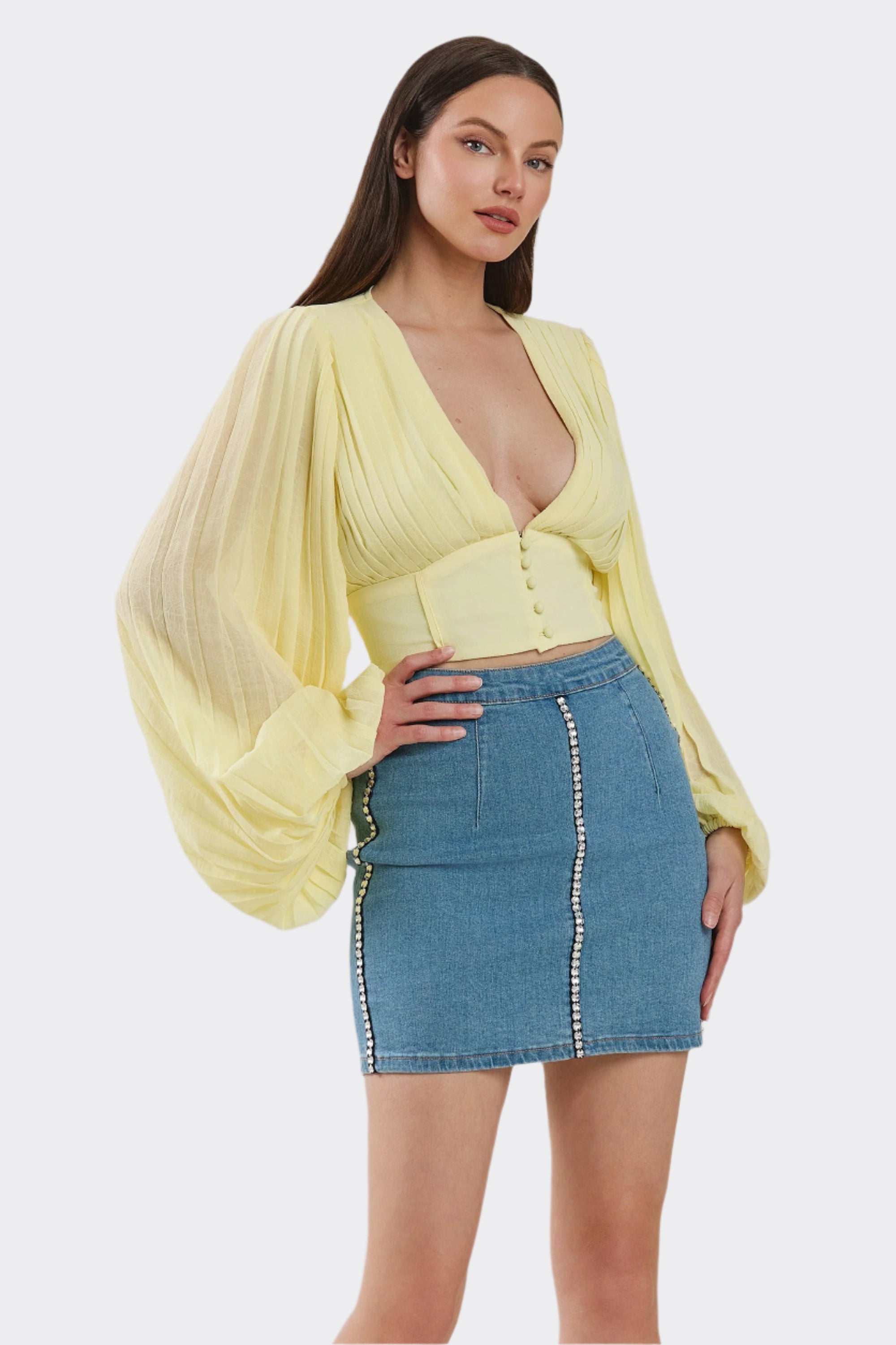 Woman wearing a yellow top and denim skirt on a plain background