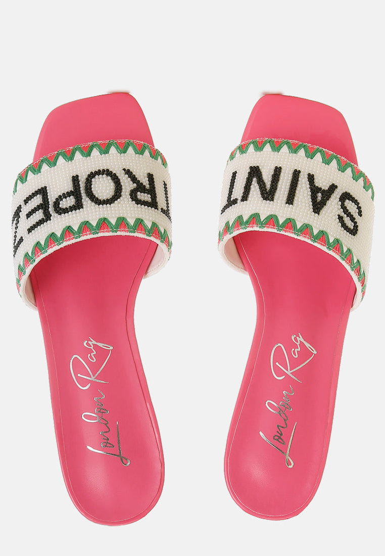 Pink sandals with 'Saint Tropez' text on a white beaded background